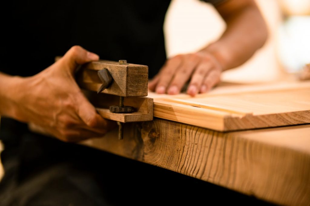 A skilled woodworker shaping wood with a hand tool in a workshop, showcasing craftsmanship and precision.
