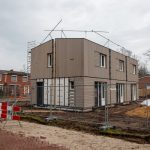 A modern house under construction with scaffolding, fences, and construction signs on a cloudy day.