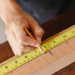 Crop anonymous male marking with pencil while measuring length of timber plank with measurement tape